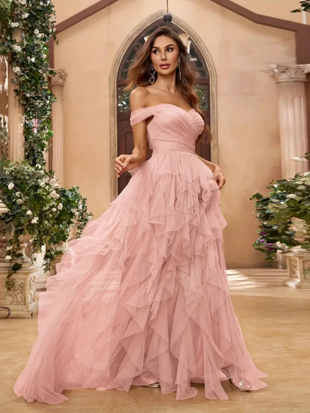 Woman in a pink off-shoulder gown standing in an elegant indoor setting with decorative elements.
